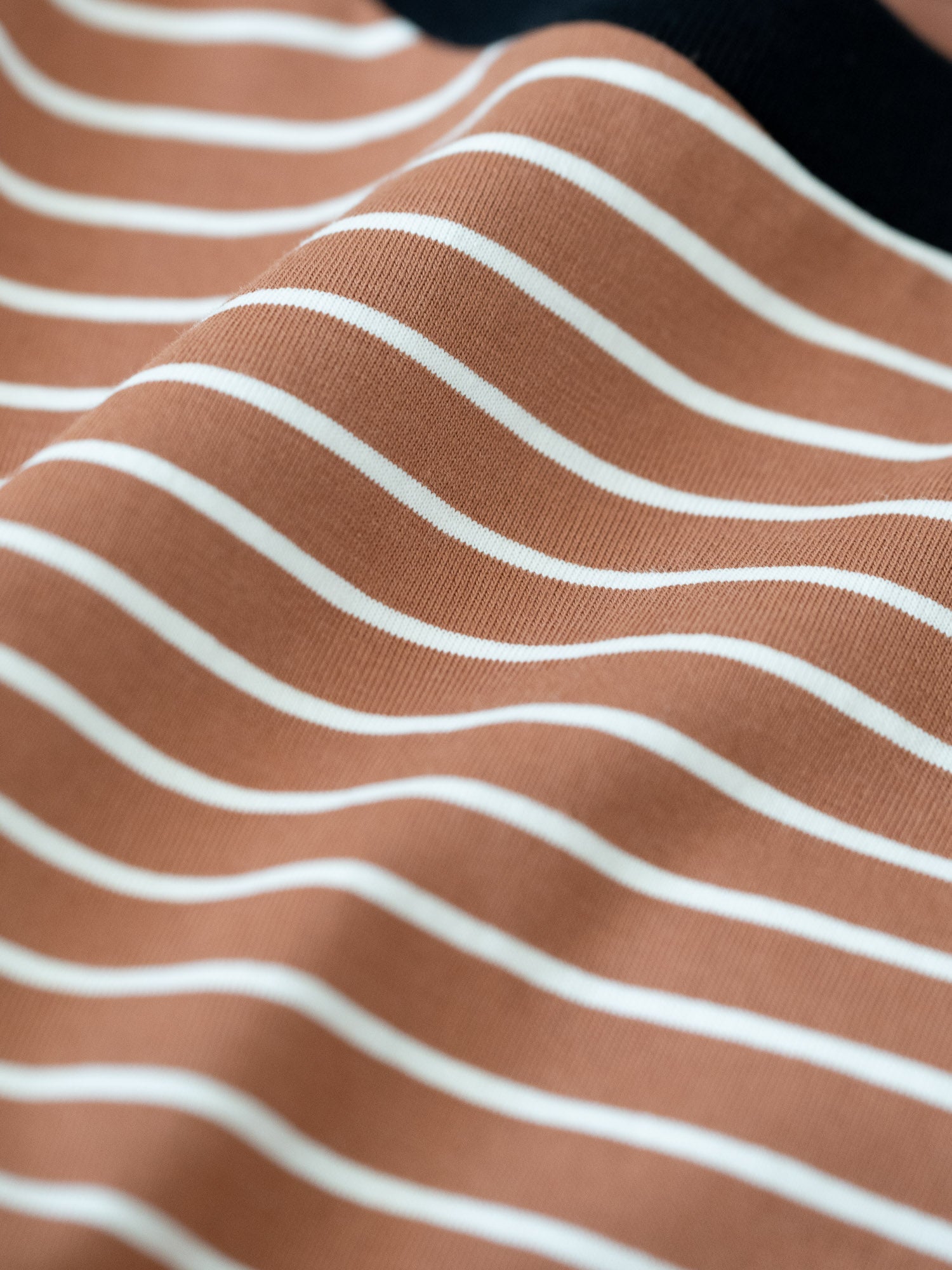 Detailansicht vom Stoff eines gestreiftes FUXBAU Fair Fashion T-Shirt aus Biobaumwolle in schwarz, weiss und karamell.