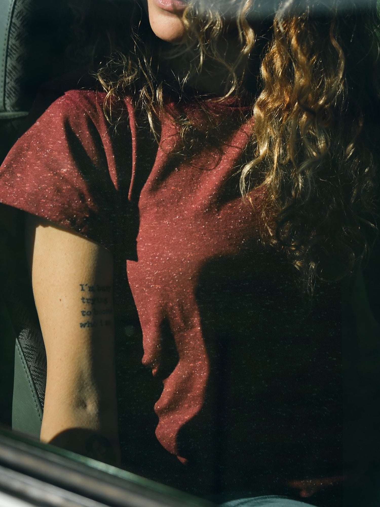 Lockige, braunhaarige Frau trägt ein bordeaux farbiges T-Shirt von FUXBAU mit weißen Punkten aus Biobaumwolle.
