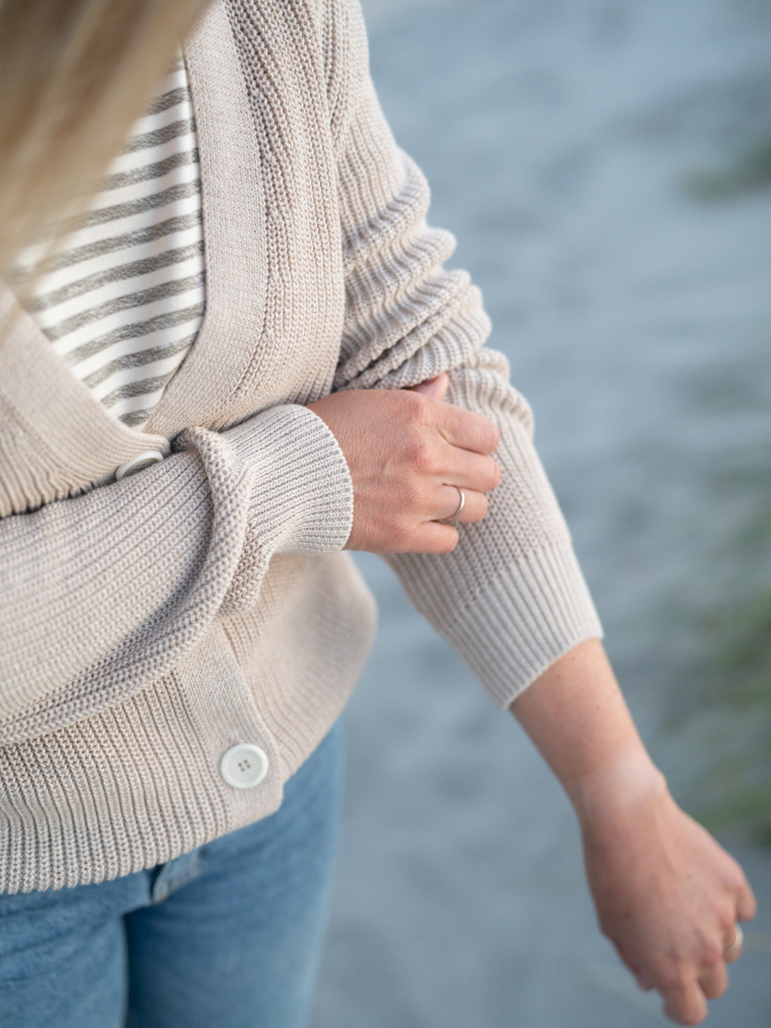 FUXBAU 4Seasons Frauen Strickjacke in beigemeliert aus 100% GOTS zertifizierter Biobaumwolle. Gefertigt in Italien und gertragen von einer jungen Frau am Strand in Portugal.