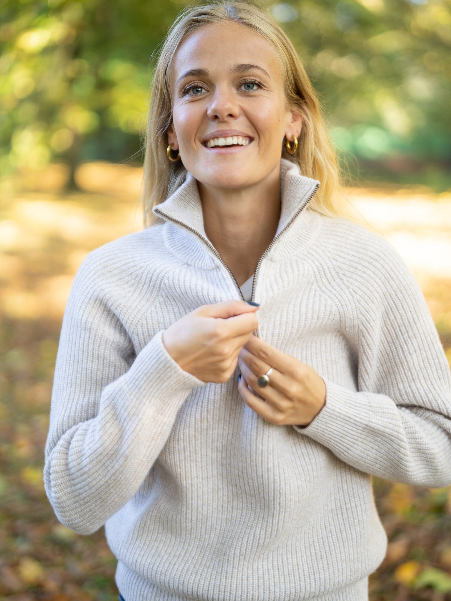 Eine junge, blonde Frau trägt einen nachhaltig und fair produzierten Fari Fashion Troyer von FUXBAU aus 100% Merinowolle in der Natur im Herbst.