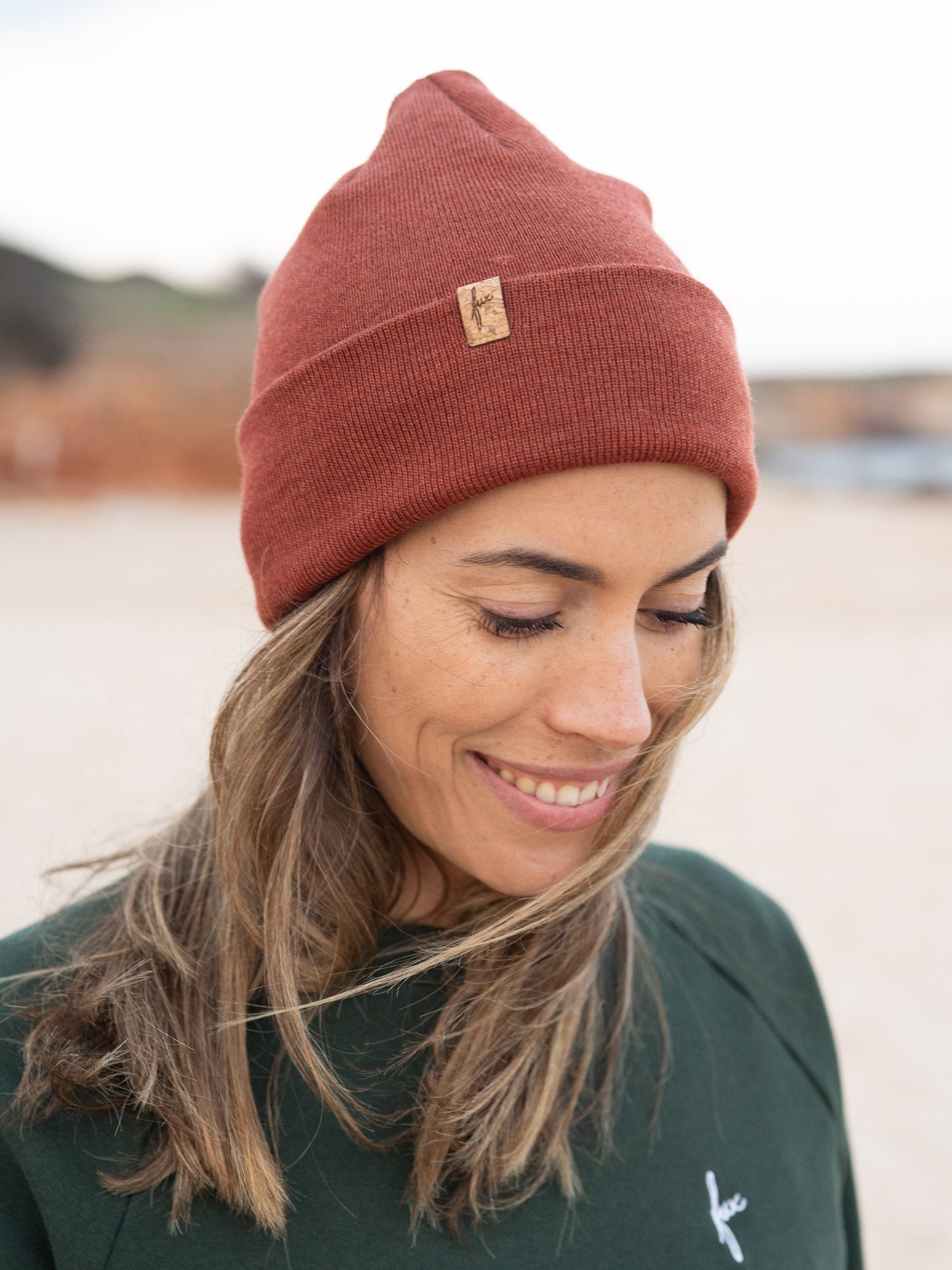 Nachhaltiger Fair Fashion Merino Kork Beanie in Herbstorange aus 100% Merino Schurwolle gestrickt in Deutschland getragen am Strand in Portugal und mit einem kleinen fux Patch aus Kork veredelt.