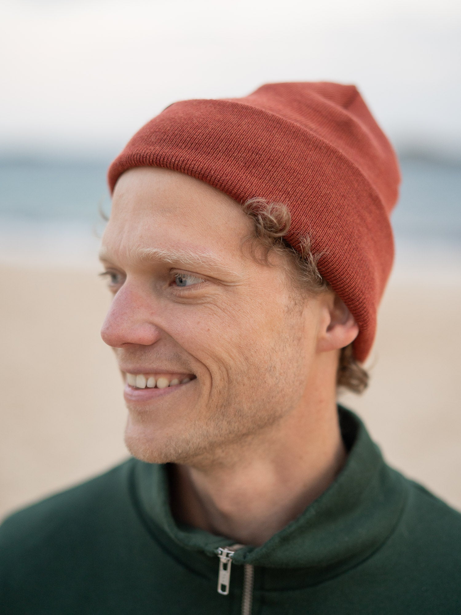 Nachhaltiger Fair Fashion Merino Kork Beanie in Herbstorange aus 100% Merino Schurwolle gestrickt in Deutschland getragen am Strand in Portugal und mit einem kleinen fux Patch aus Kork veredelt.