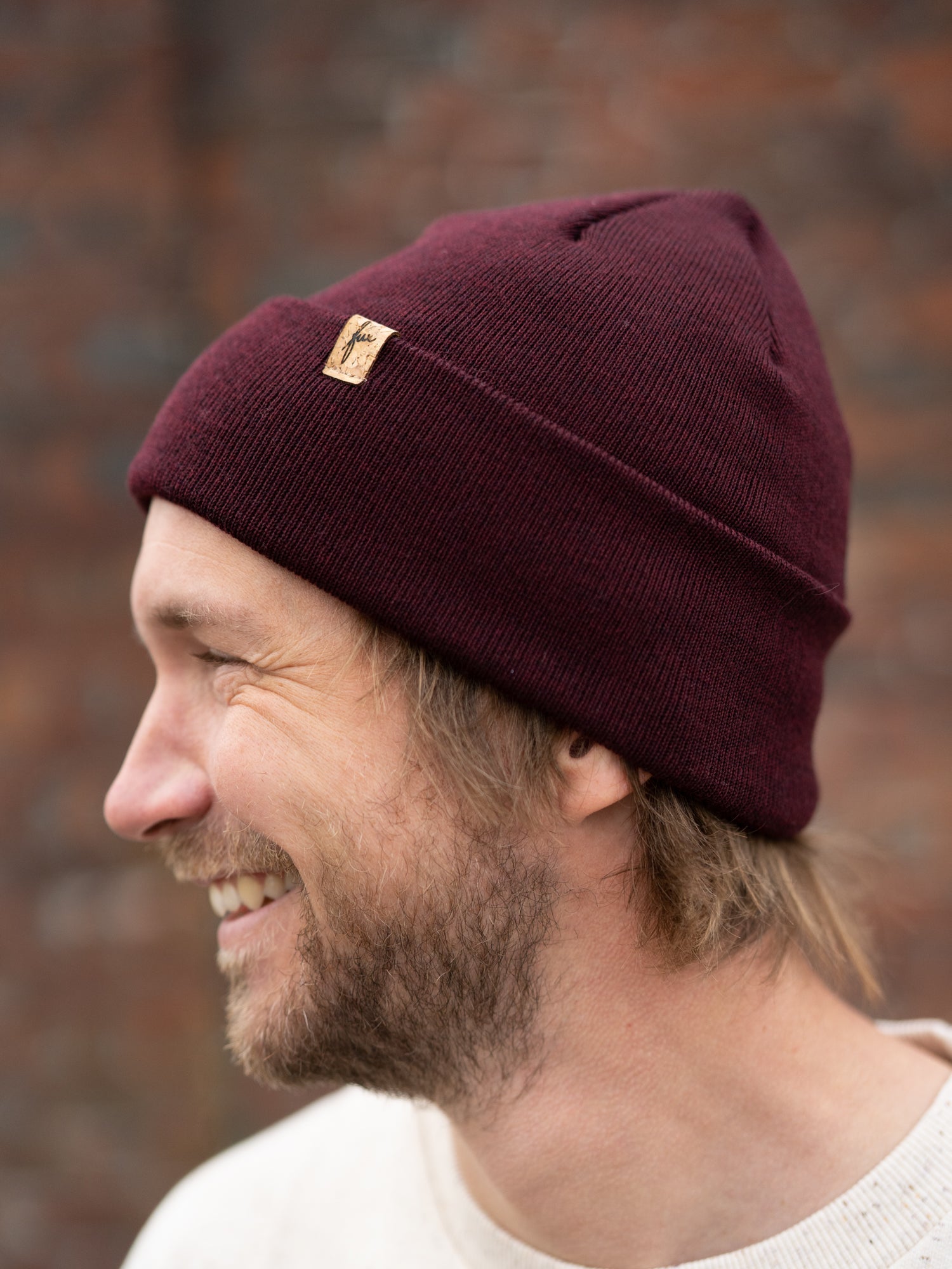 Kenny trägt eine nachhaltig Fair Fashion FUXBAU Merino Kork Beanie aus Merino Schurwolle gestrickt in Deutschland in Bordeaux.